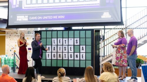 Holmes Murphy employees reveal a Wheel of Fortune-inspired board that says Let's Raise A Fortune in honor of United Way Week