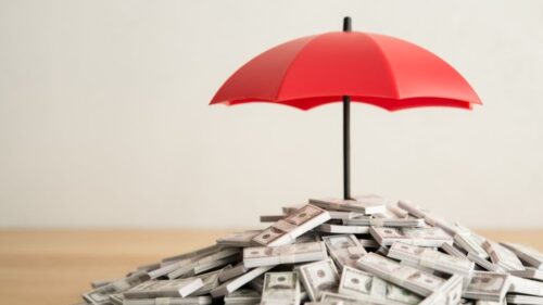 A red umbrella representing umbrella insurance coverage covers a pile of cash
