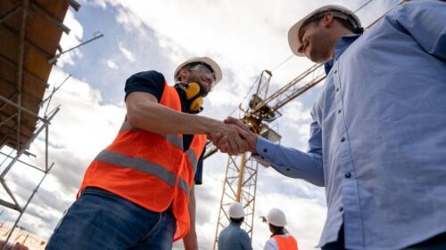 Two people in hard hats shake hands on a construction site