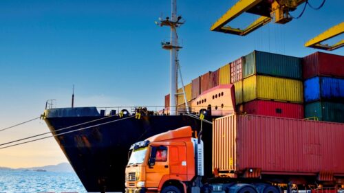 An orange semi-truck and colorful container ship
