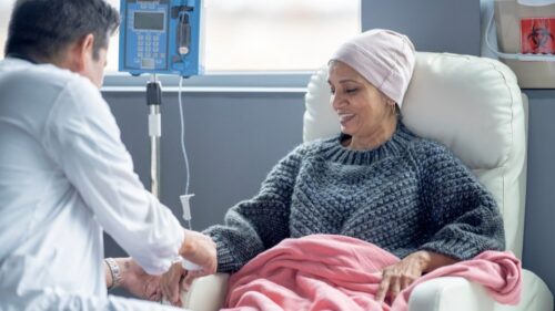 A cancer patient looks at her hand while a doctor connects an IV with treatment