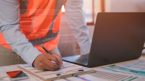 A contractor in an orange vest reviews data and blueprints.