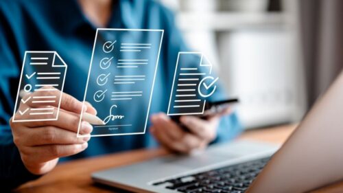 A digital contract concept hovers in front of a person signing the contract while looking at their phone and laptop.