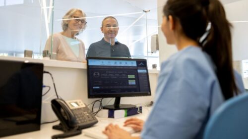 A nurse greets two patients and checks them in on the computer
